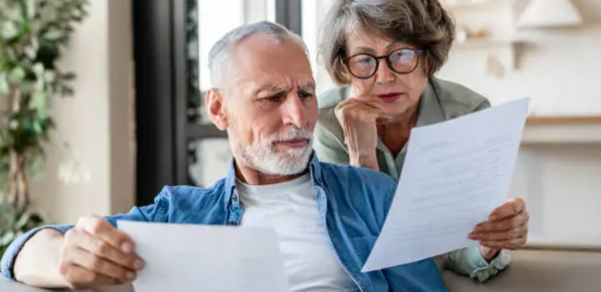 노부부가 집 안에서 서류를 함께 검토하며 심각한 표정을 짓는 모습.