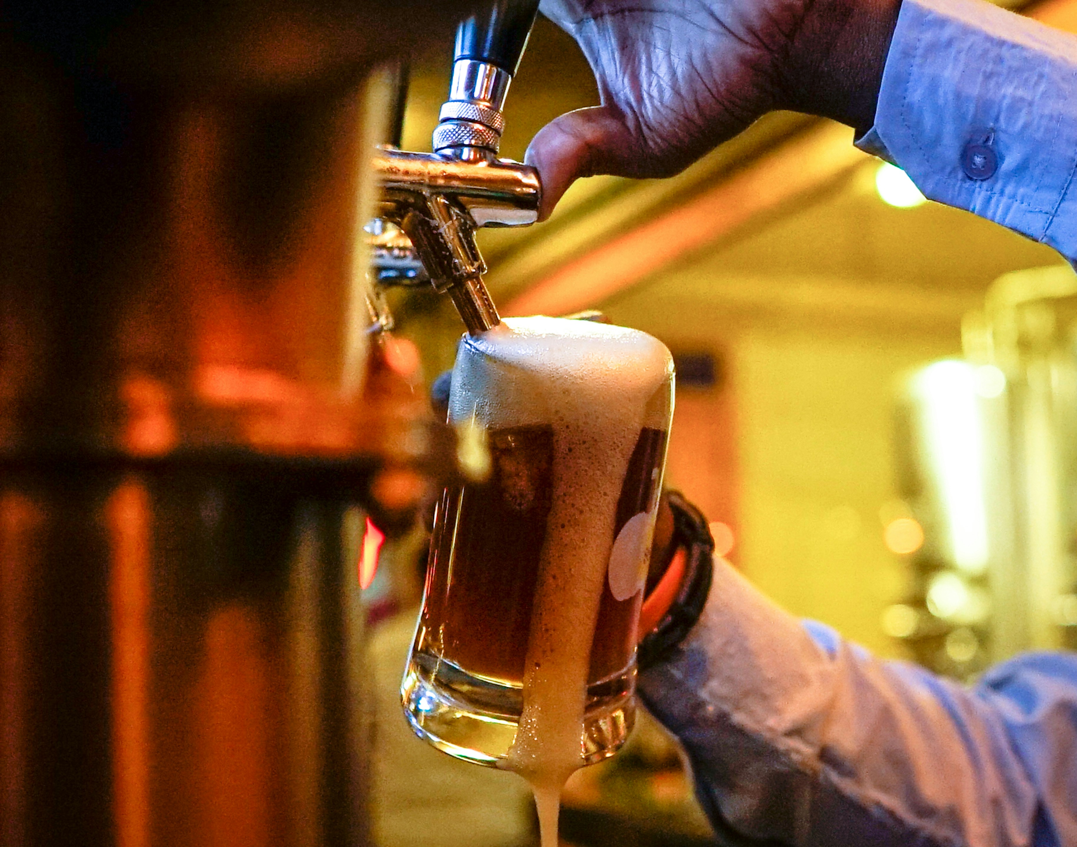 맥주를 따르는 기계에 생맥주 잔을 대고 맥주를 가득 따르고 있는 남성의 사진