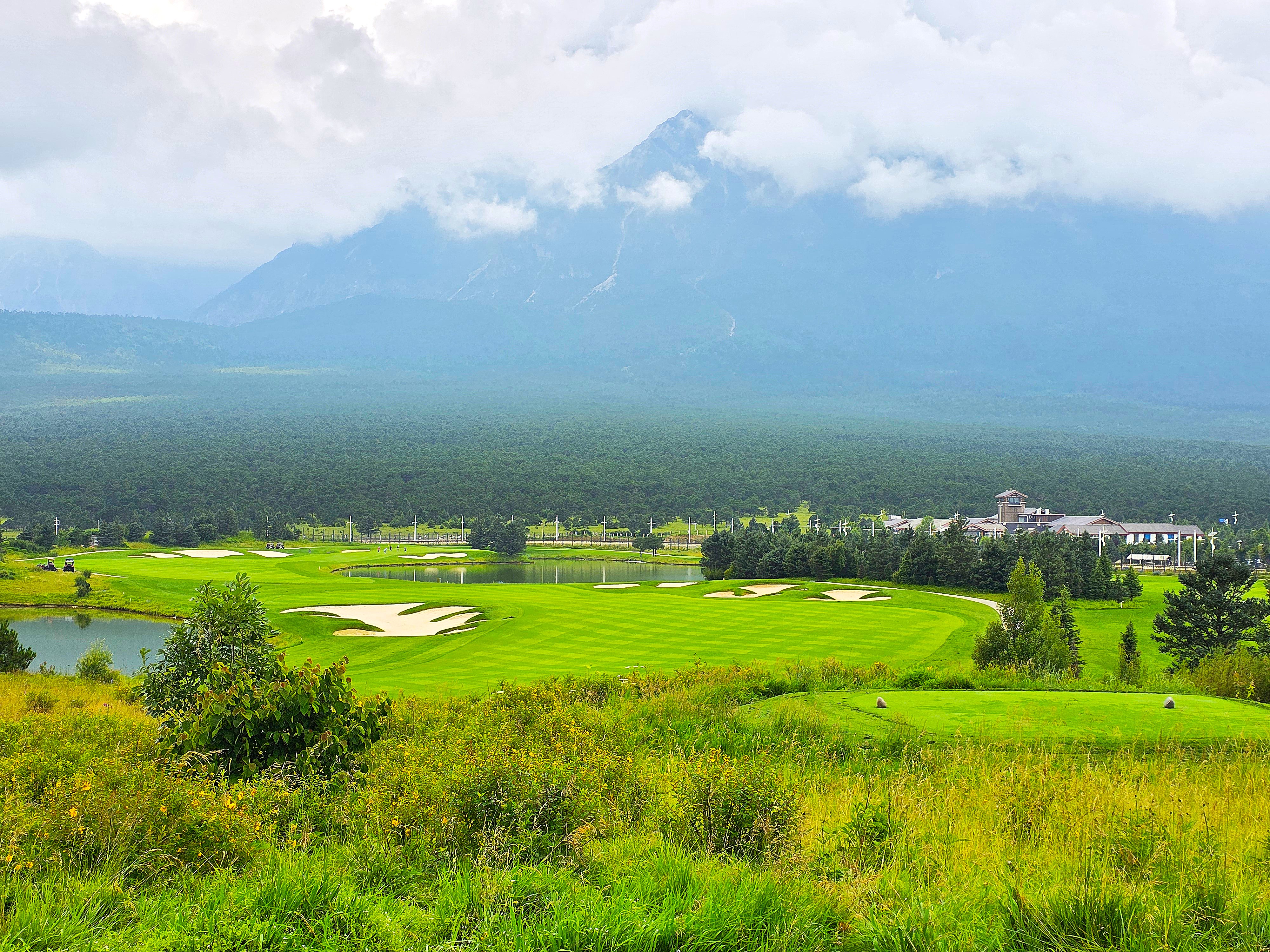 중국 운남성 여강 옥룡설산 골프장의 페어웨이와 그린, 그리고 뒤로 펼쳐진 옥룡설산의 웅장한 풍경. 아름답게 관리된 골프 코스와 설산의 조화.