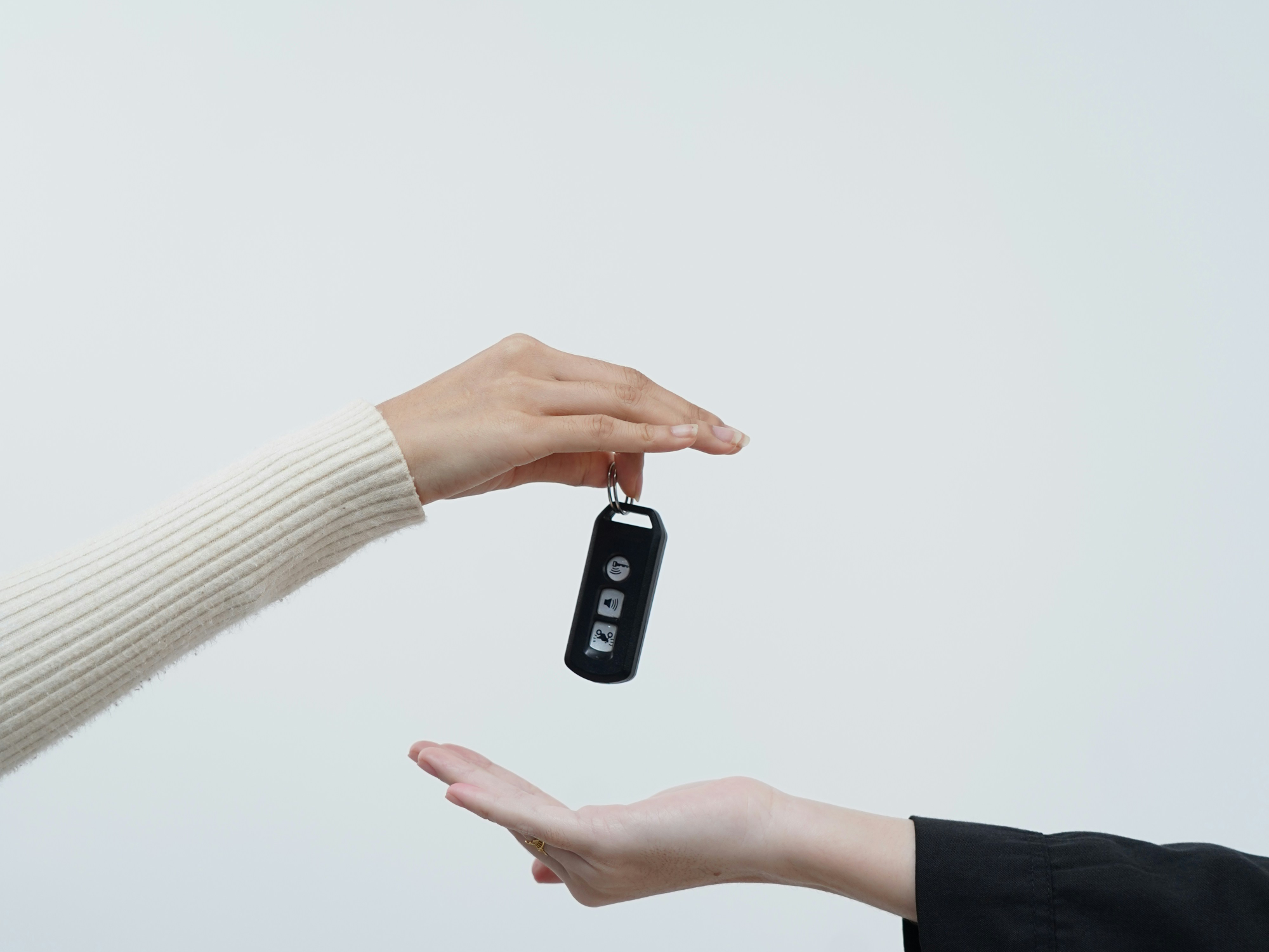 흰색인 공간에서 두 손이 서로 차 키를 서로 주고받으며 차량을 구매하고 있다.