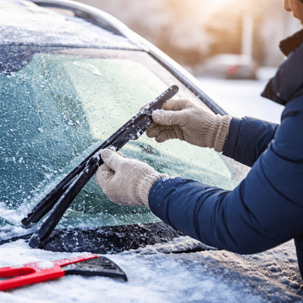 와이퍼가 얼어붙은 겨울 아침, 장갑 낀 손으로 앞유리 와이퍼를 조심스럽게 들어 올리는 모습