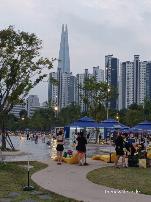 롯데타워를 배경으로 해질 무렵 시민들이 물놀이 준비를 하는 잠실 한강공원 수영장