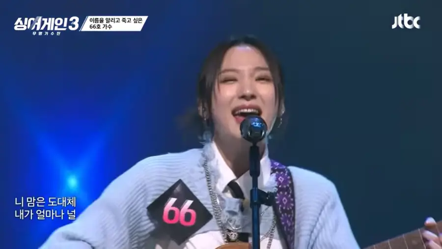 싱어게인3- 하늘색 자켓을 입고 기타를 치며 스탠딩마이크 앞에서 웃으며 노래하는 66호