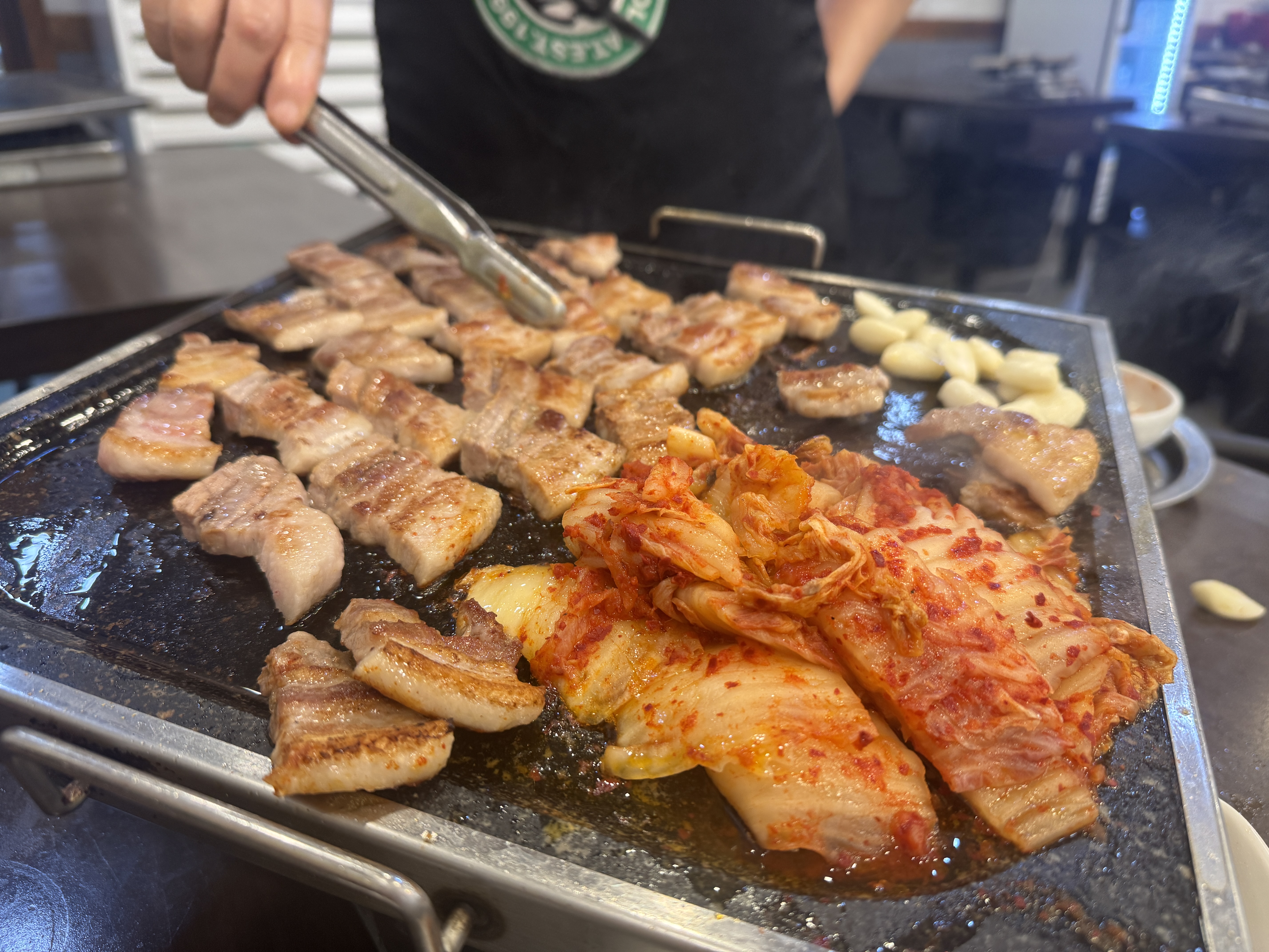 노릇노릇하게 익은 삼겹살과 구운 김치&amp;#44; 통마늘이 돌판 위에 골고루 익어가는 모습. 먹음직스럽게 갈색으로 구워졌다.