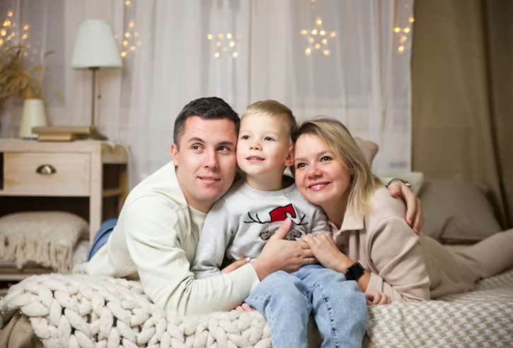 포근한 침실에서 함께 앉아 웃고 있는 부모와 어린 자녀의 모습