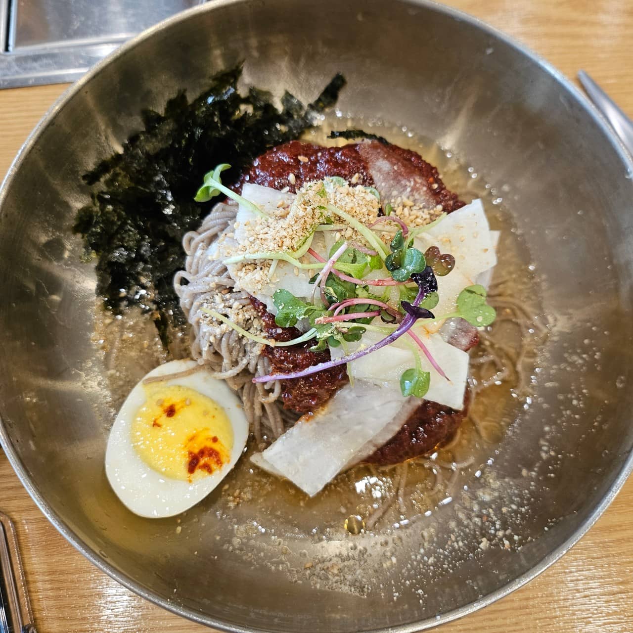 '개수리막국수' 비빔막국수 사진입니다. 냉면그릇 안에는 메밀면과 함께 김가루, 양념장, 무절임, 새싹채소, 삶은계란이 올려져 있습니다.