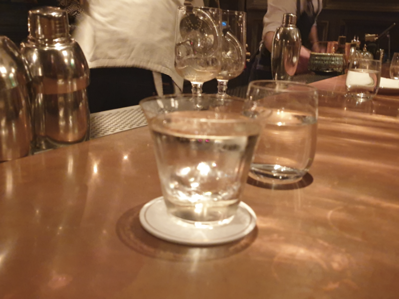 우드 테이블 위에 물 컵 하나와 칵테일 잔 하나가 올려져 있다.