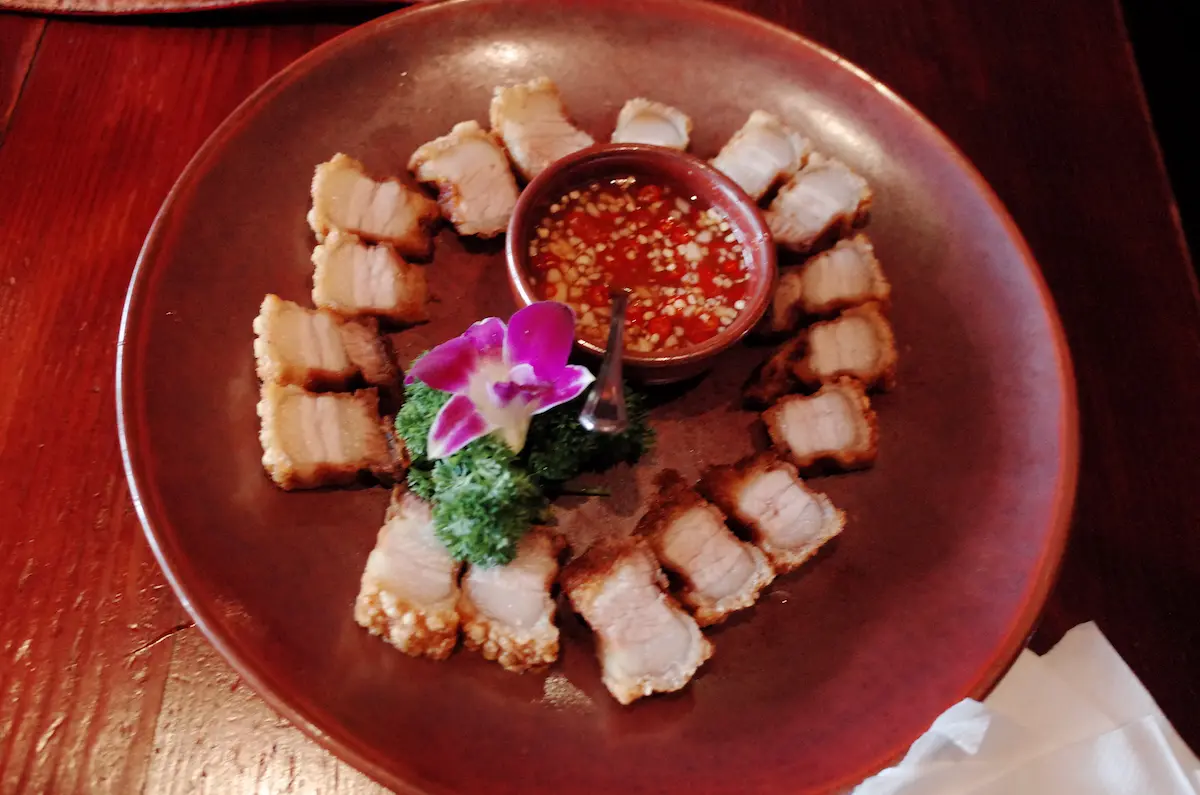 꽃 장식과 함께 원형으로 플레이팅된 로스트 헤븐의 겉바속촉 크리스피 포크 벨리 요리