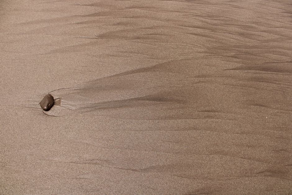 Close-up view of textured sand with a single pebble creating a ripple effect.