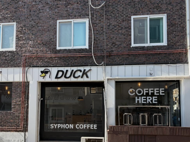 적벽돌 건물에 회색 간판 그리고 큰 유리창을 가진 카페