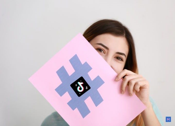 틱톡 해시태그 전략을 보여주는 핑크색 해시태그 보드를 들고 있는 여성 크리에이터, 틱톡 로고가 중앙에 배치된 모습 via Canva