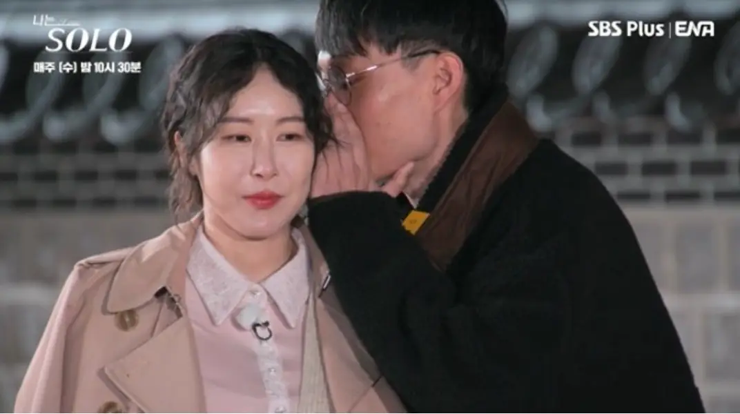 나솔-검은옷을 입고 흰색 바바리를 입은 순자에게 귓속말을 하고있는 광수