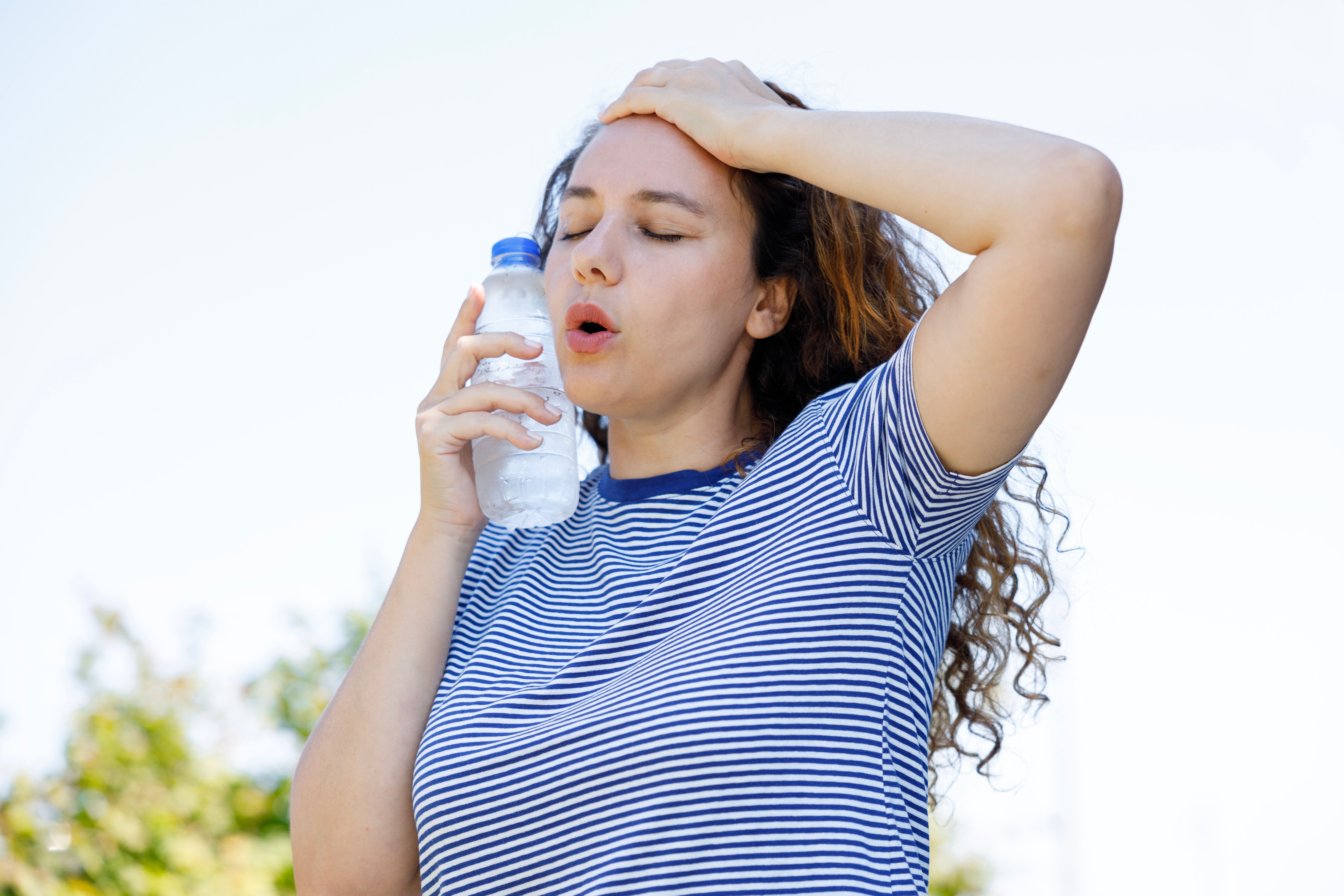 무더위 속 피부 온도를 식히기 위해 이마에 손을 얹고 물병을 얼굴에 대고 있는 여성