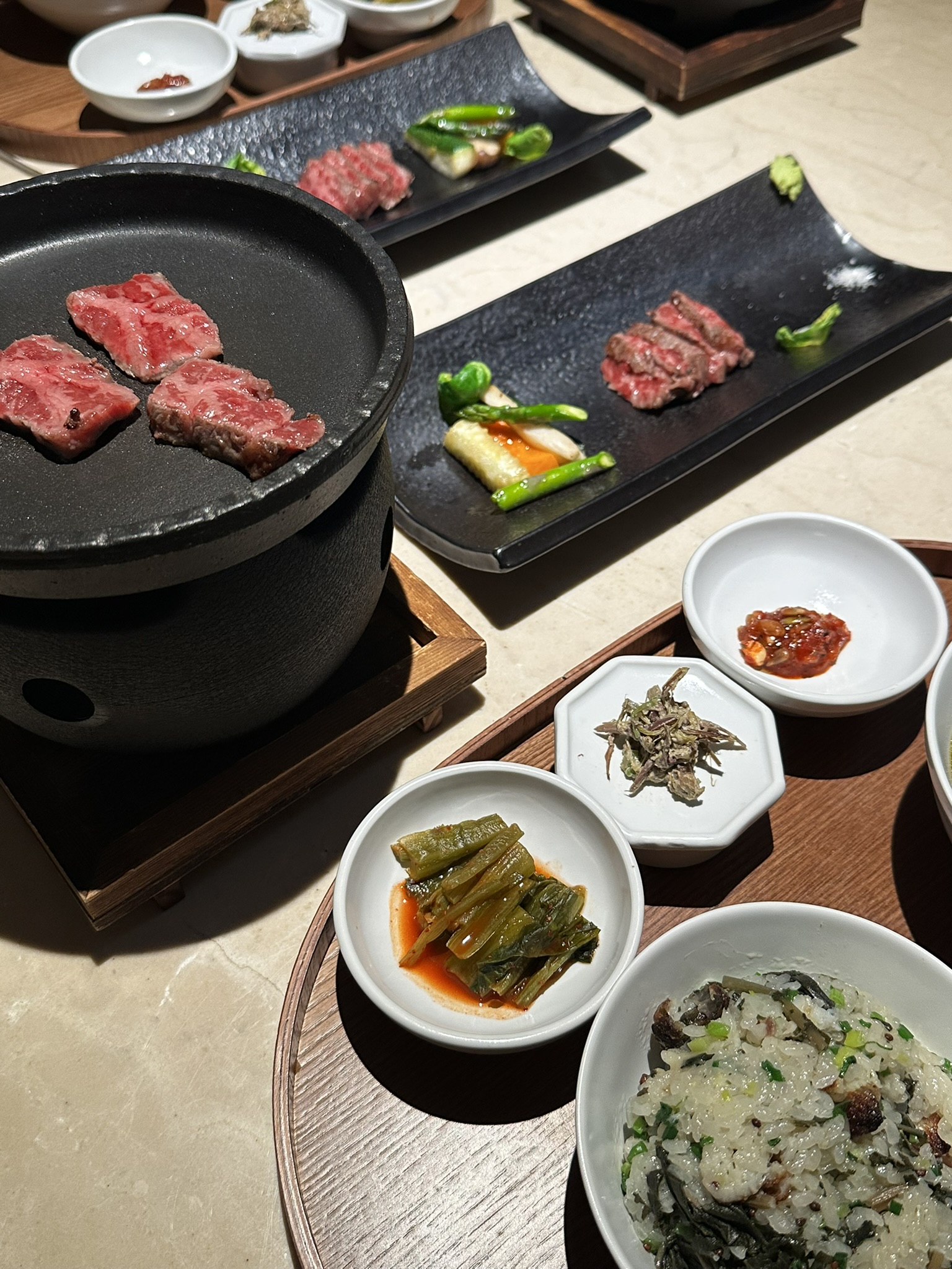 화로에 한우 구이가 구워지고 있고, 농어 솥밥 반상이 차려져 있는 사진