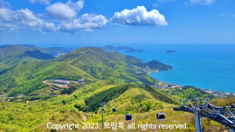 카이블카가 운행되는 모습. 파란하늘에 하얀구름이 걸려있고 푸른 바다 왼편에는 연두빛 산이 보인다.