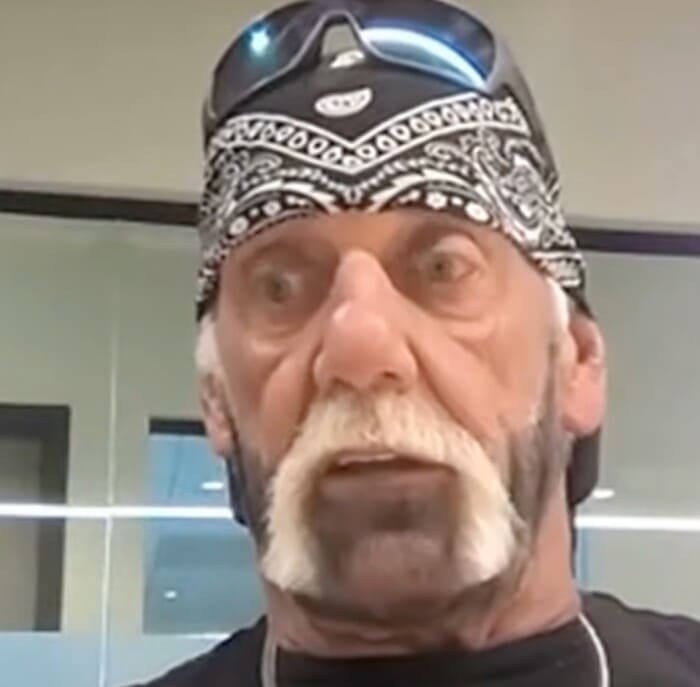 검정색 반다나와 선글라스를 착용한 헐크 호건이 실내 공간에서 인터뷰 중인 모습. 회색 수염과 진중한 표정이 인상적이다.