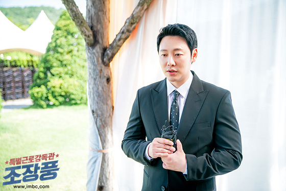 검은 정장을 입고 촬영용 마이크 장비를 든 조진갑 역 김동욱