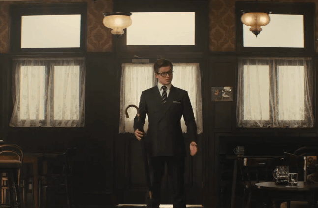 A smartly dressed young gentleman stands inside the cafeteria door holding an English umbrella.