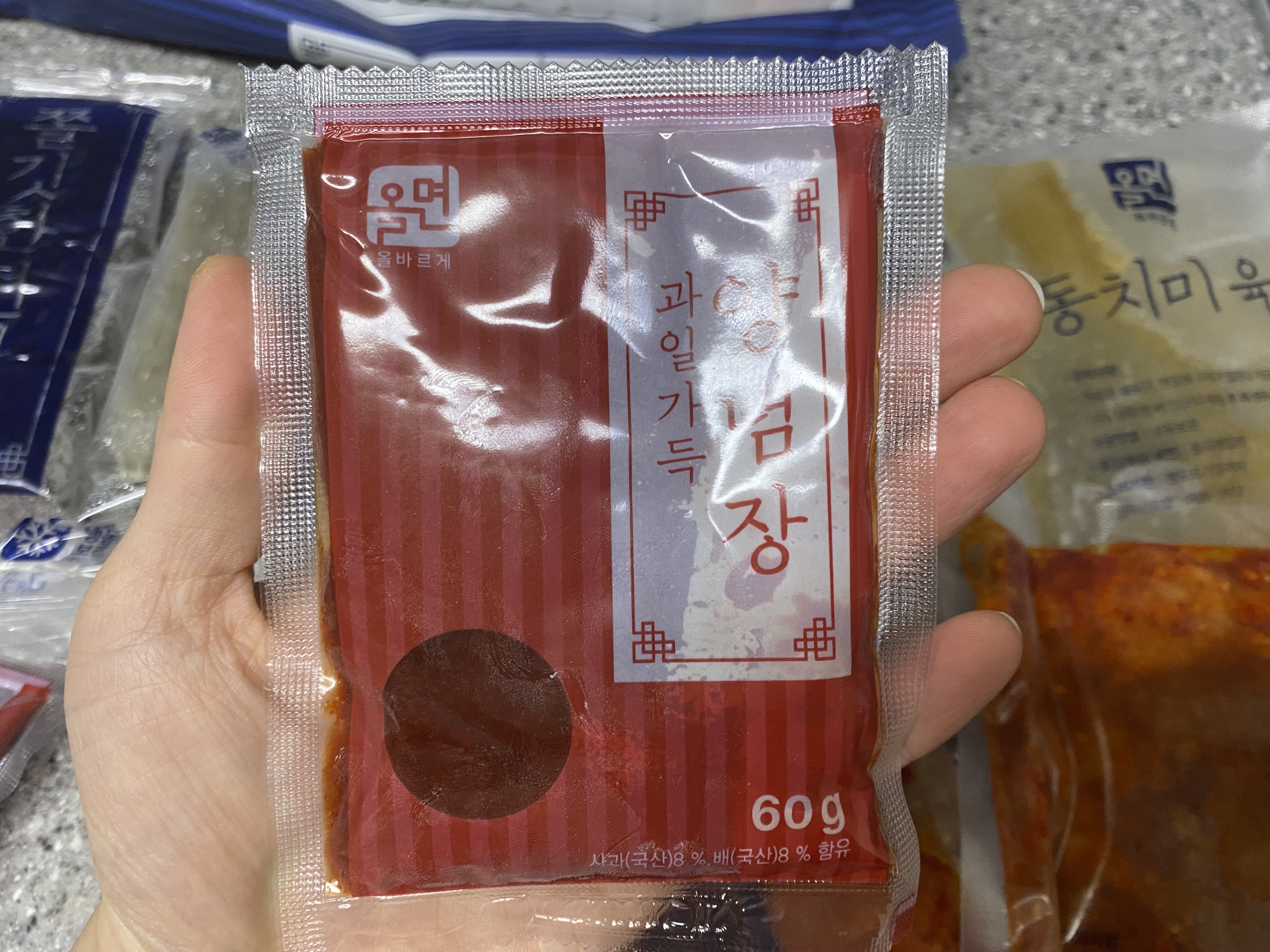 과일 양념장을 손에 들고 있는 사진입니다 빨간색 봉지의 과일양념장은 60g입니다.