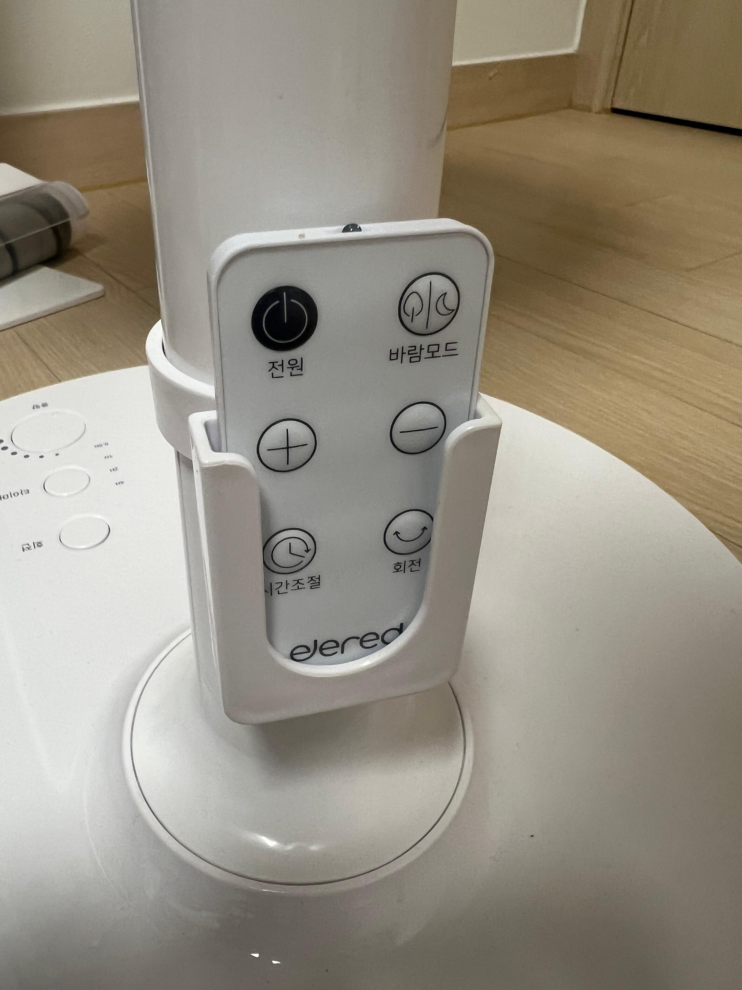 일레드 EDF-2414W 리모컨 베이스 거치대 수납 모습 &mdash; 흰색 사각 리모컨이 선풍기 베이스 원형 홀에 꽂혀 있음