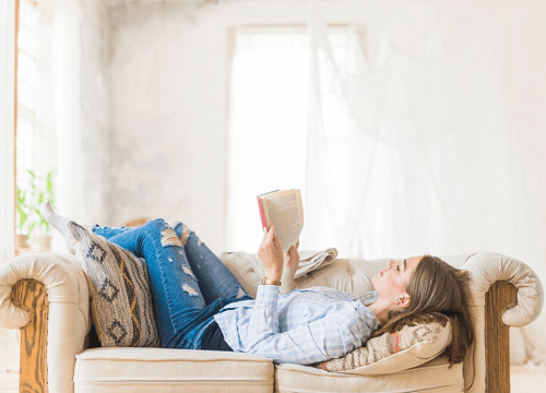 쇼파에 누워 책을 읽고 있는 여성