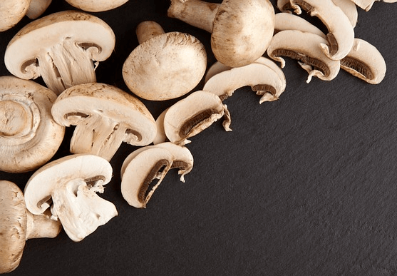 검정 도마에 하얀 양송이들이 가득하다. 동그란 버섯과 반으로 잘린 버섯, 얇게 잘린 버섯 슬라이스들이 있다.