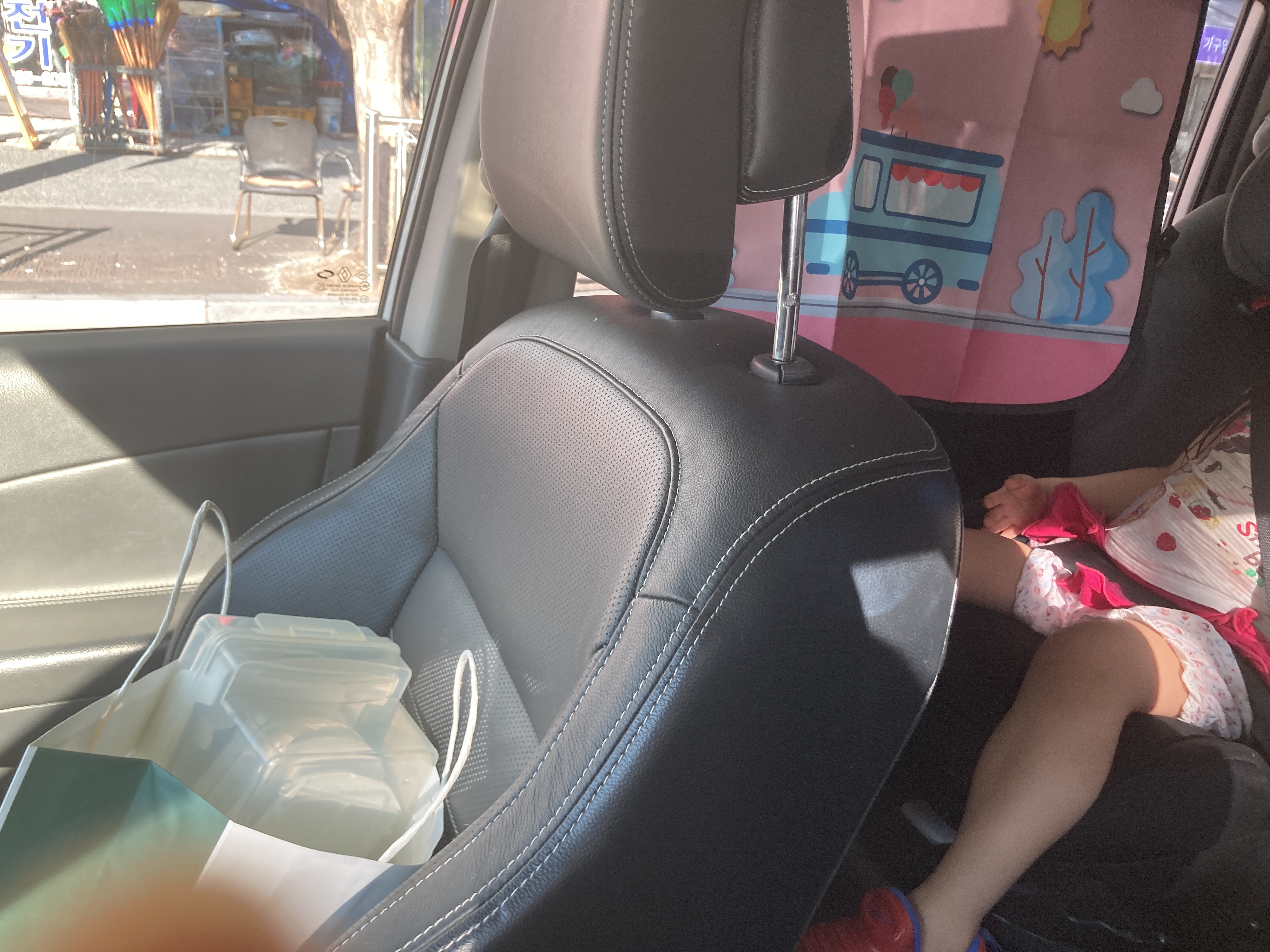 핑크색 디자인 햇빛가리개가 차량 뒷좌석 창에 설치되어 있고, 카시트에 앉은 아이 다리가 보이는 모습