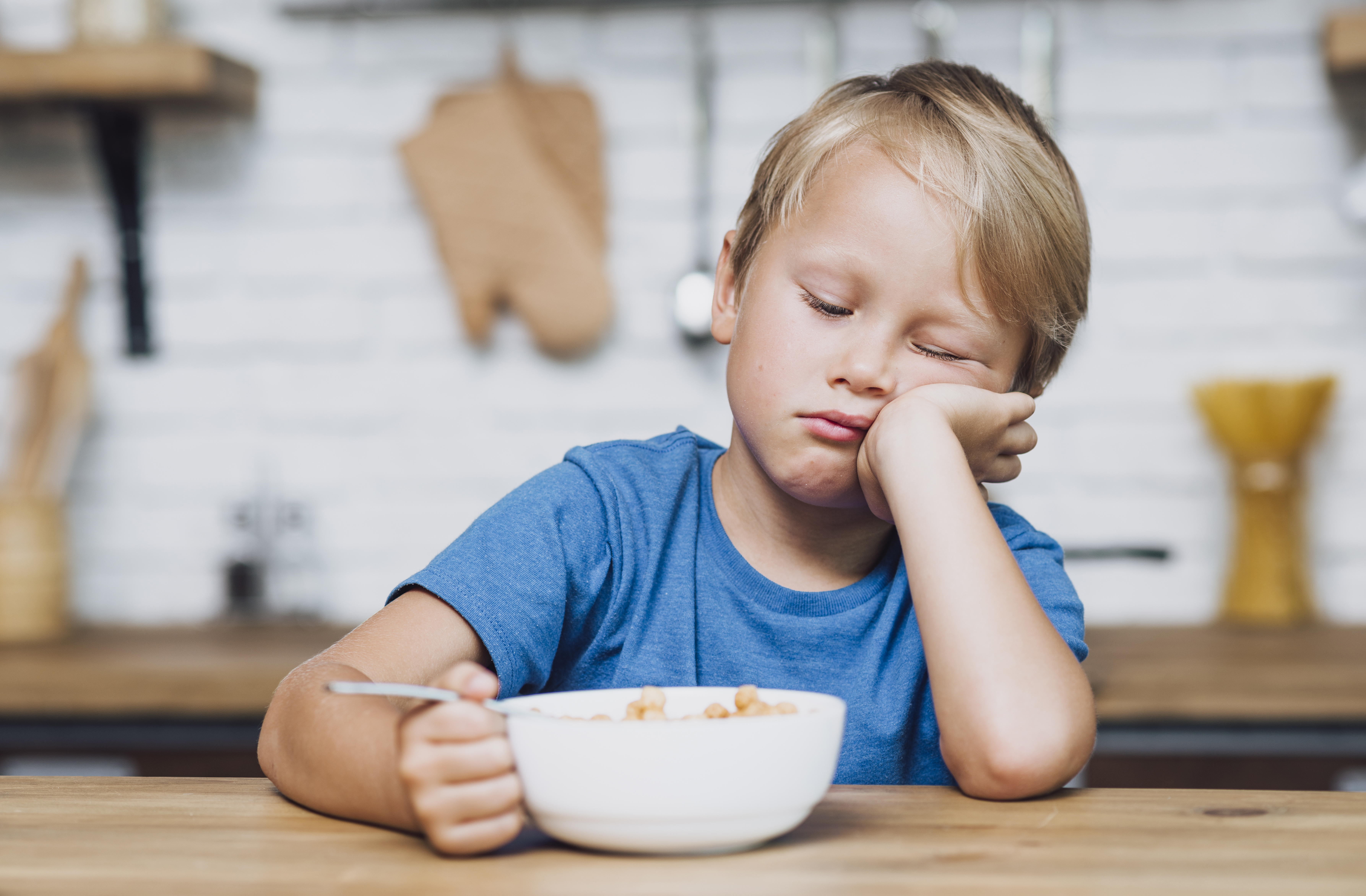 식탁에는 앉아 있지만, 먹기 싫어하는 아이 사진 (front-view-tired-boy-trying-eat-his-cereals)