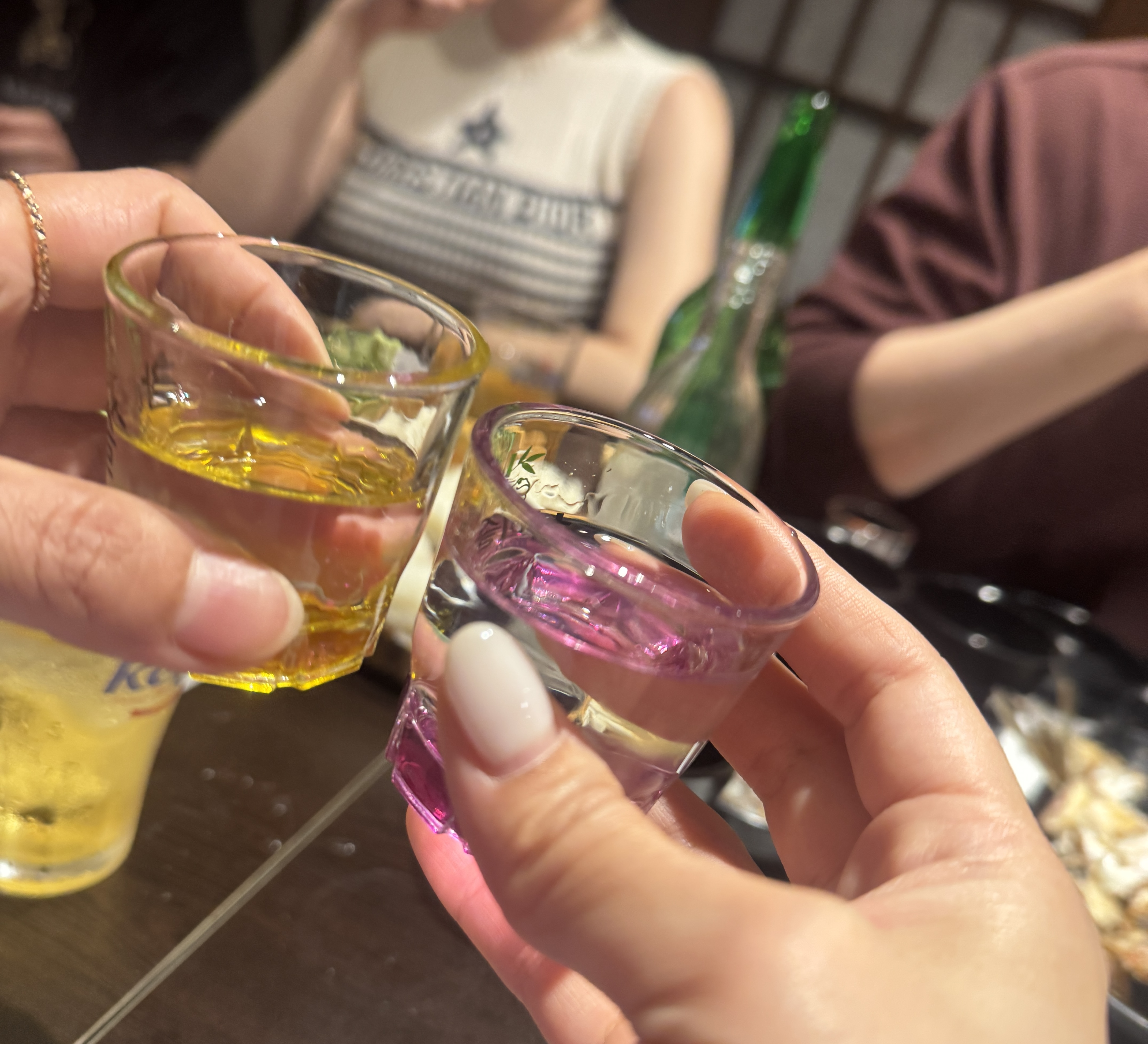 색색의 샷잔으로 서로 짠하는 장면. 노란색과 분홍색의 술잔이 손에 들려 있어 시각적으로도 재미를 준다.