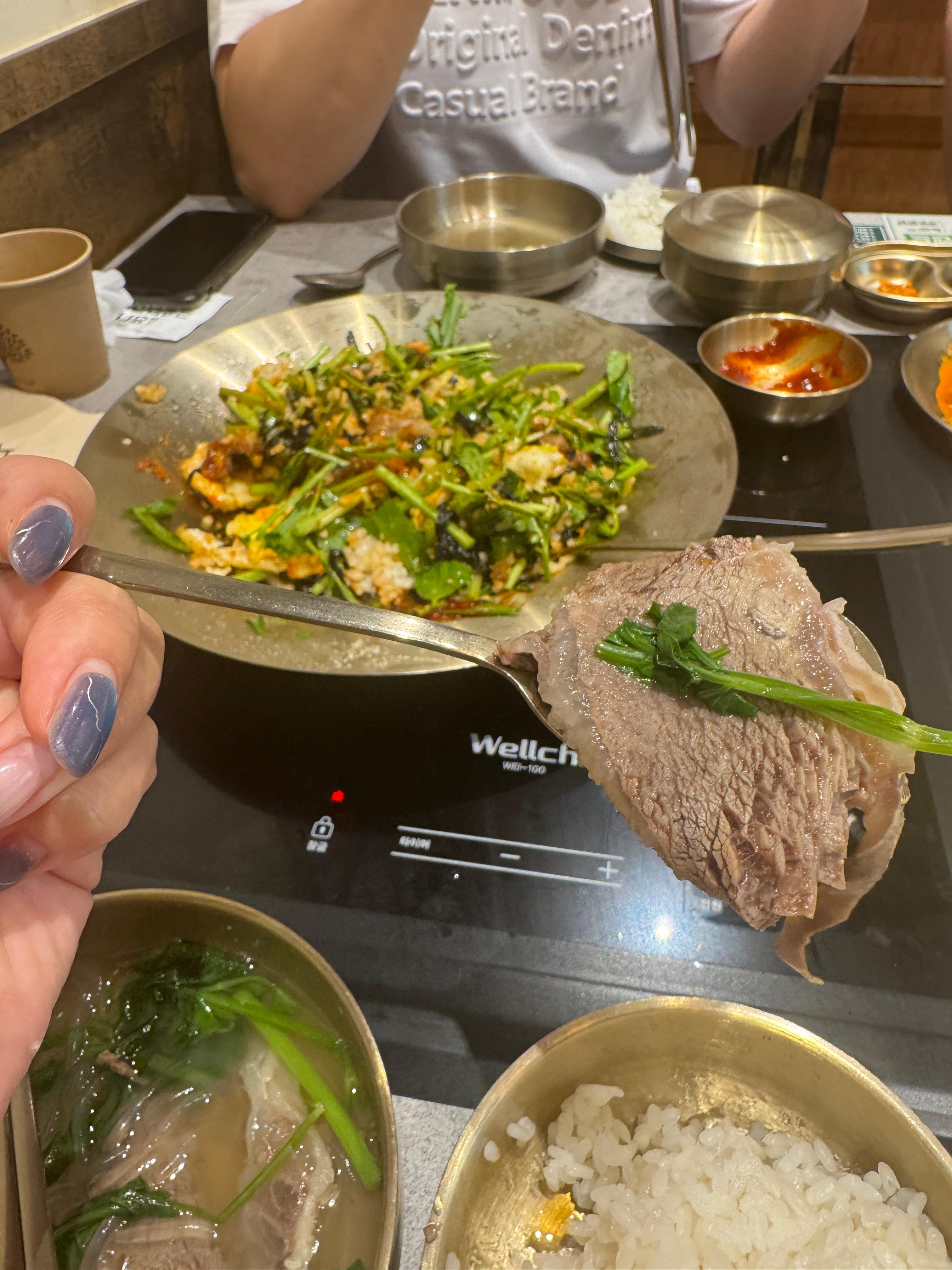 손에 든 숟가락 위 소고기와 미나리&amp;#44; 테이블엔 국물&middot;밥&middot;비빔밥이 함께 놓인 장면