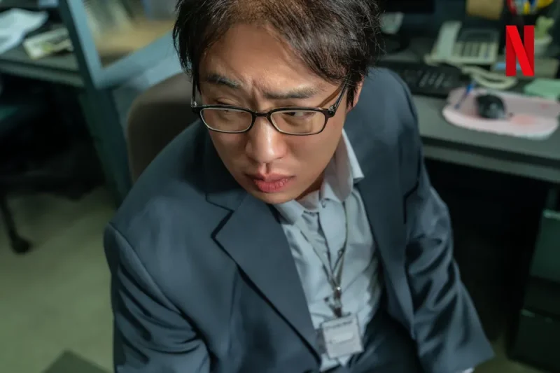 대머리에 안경을 쓰고 회색 양복을 입고 있는 마스크걸의 주오남