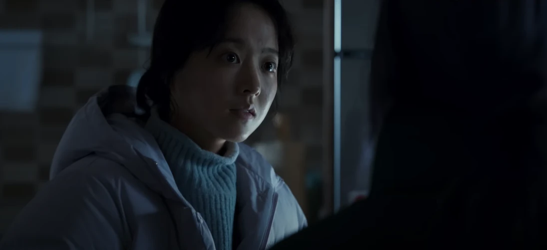 어느 실내에서 흰색 패딩을 입고 의문스러운 표정으로 이야기를 듣고 있는 박보영