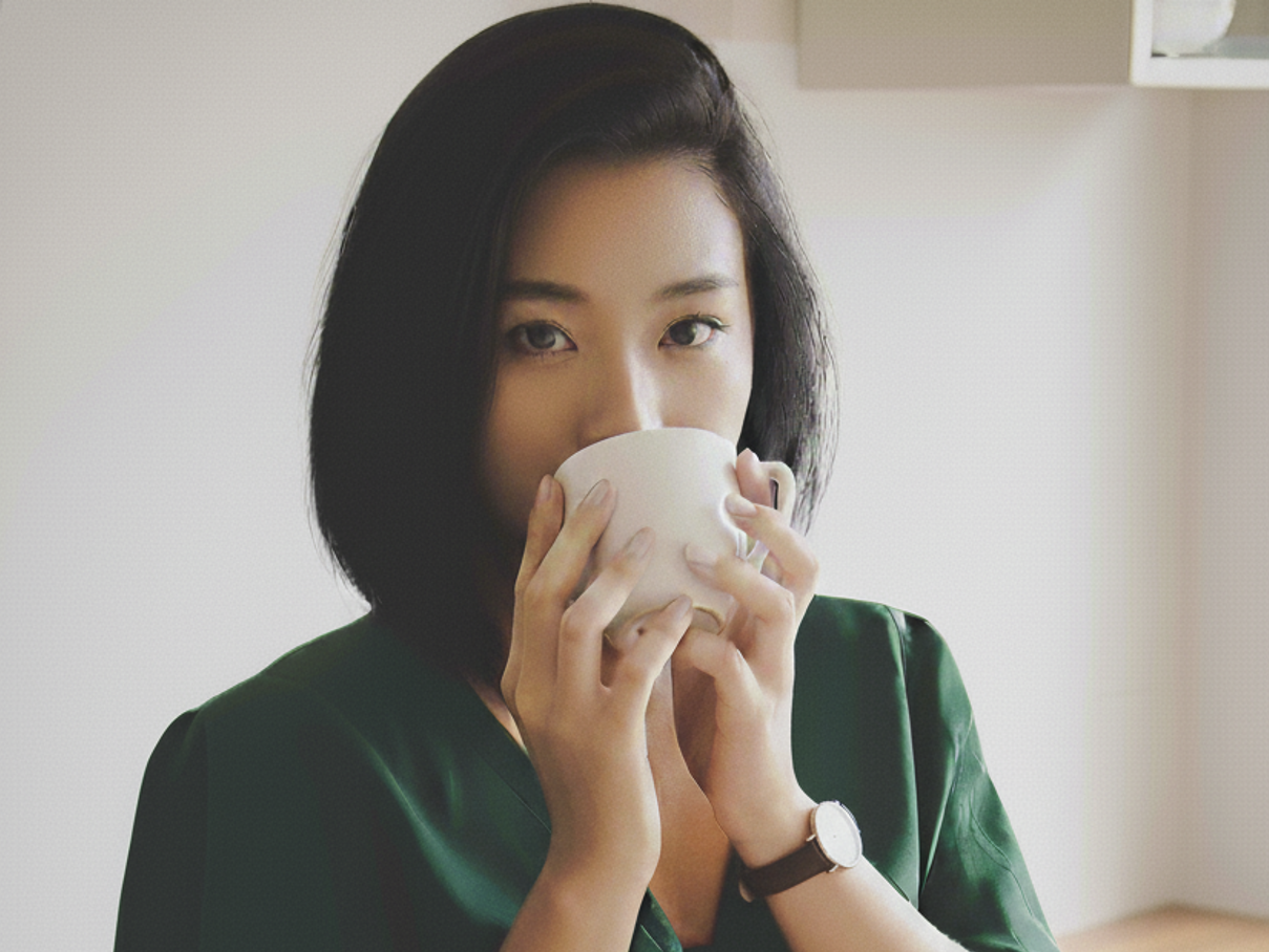 초록색 옷을 입은 여자가 커피 잔을 들고 커피 향을 맡고 있다.