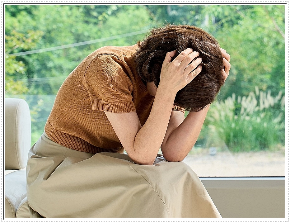 고개를 숙인 채 양쪽 머리를 부여잡은 여성의 모습