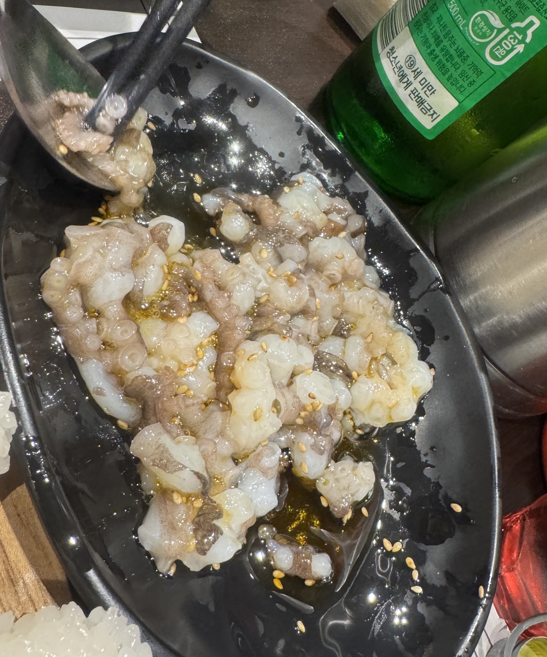 물고기 자리 논현점에서 제공된 낙지 탕탕이. 잘게 썬 산낙지가 참기름과 깨소금에 버무려져 검은 접시에 담겨 있다.