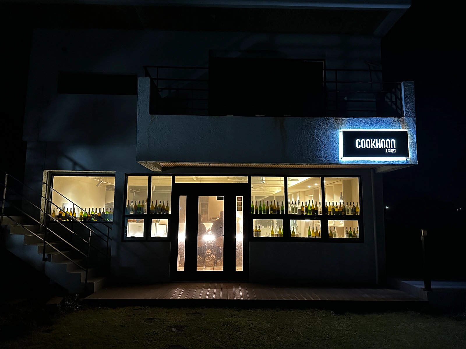 제주-구좌읍-평대리에있는-숨은맛집-쿠쿤-저녁시간에찍은-어두운외관이다-쿠쿤이라는-간판이보이고-안에는눈이편안한노란불빛-창가에는-와인병들이-진열되어있다