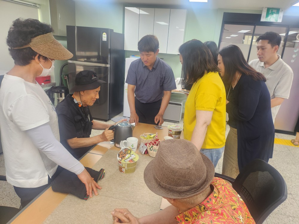이미지설명: 농심 직원들이 시각장애인쉼터 이용인들에게 컵라면 용기와 조리법에 대해 설명하고 있다.