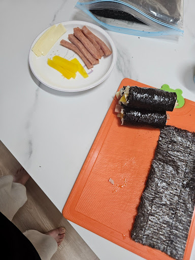 주방 도마 위에서 갓 만든 김밥과 치즈, 햄, 단무지 등 김밥 재료들.