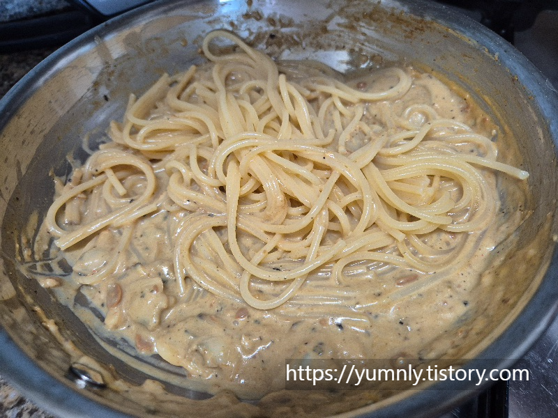Mixing spaghetti noodles with the creamy doenjang and clam sauce in a pan