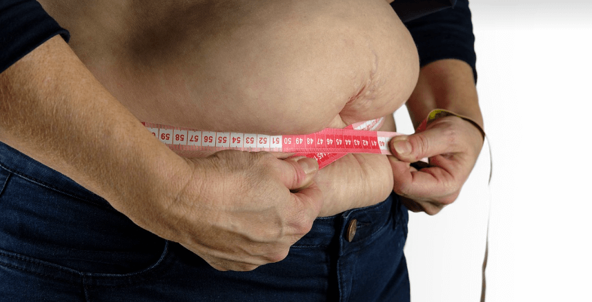 복부 비만인 남자가 허리 사이즈를 줄자로 재고 있는 모습