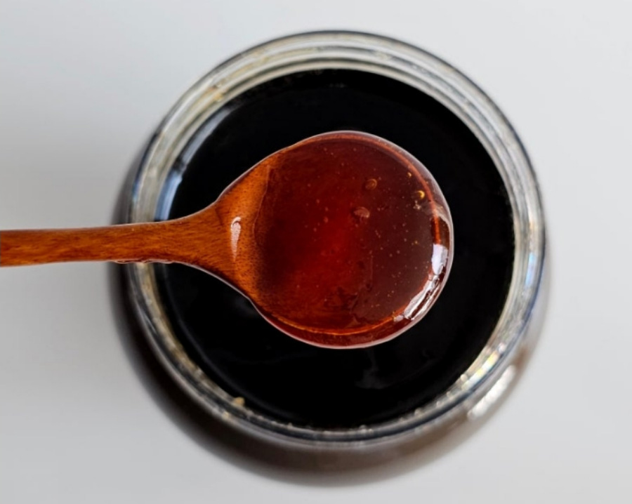 야생에서 채취를 한 매실을 엑기스로 만든 것을 동그란 유리병에 가득 담아 놓은 것을 나무 숟가락으로 한숟가락 떠 놓은 것을 유리병 입구에 걸쳐 놓은 것을 찍은 사진