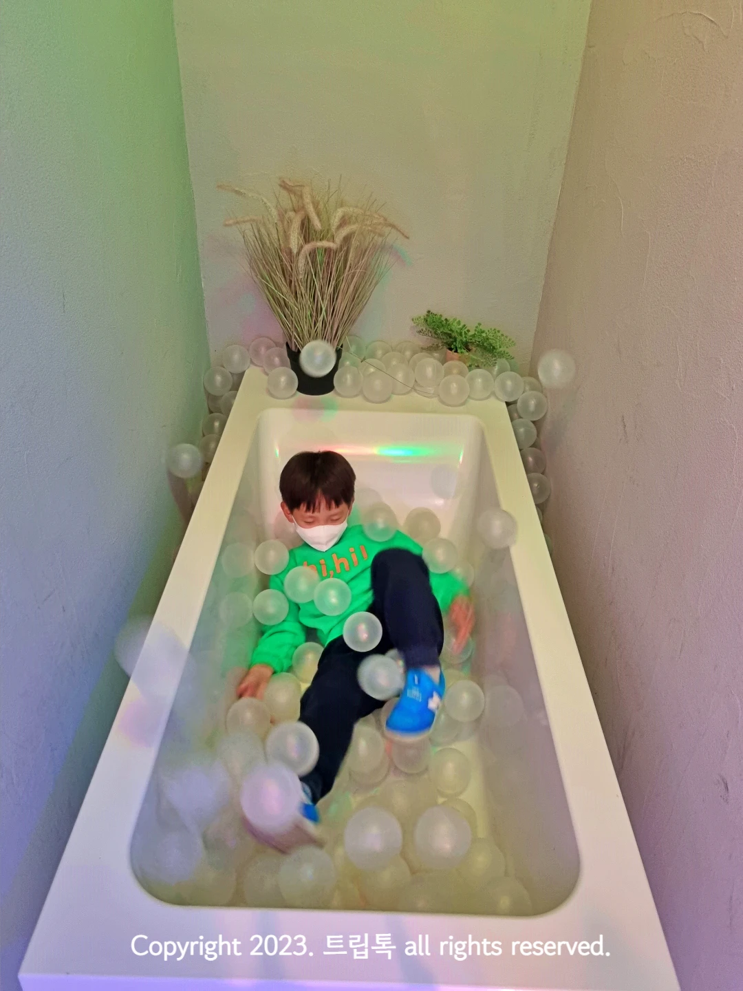 하얀 욕조에 투명한 공이 있고 아이가 누워있다.