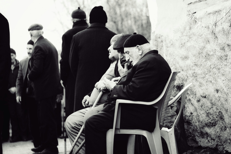 서양의 노인들이 야외의 의자에 앉아서 옆사람과 손에 든 것을 보면서 얘기를 하고 있는 것을 찍은 사진