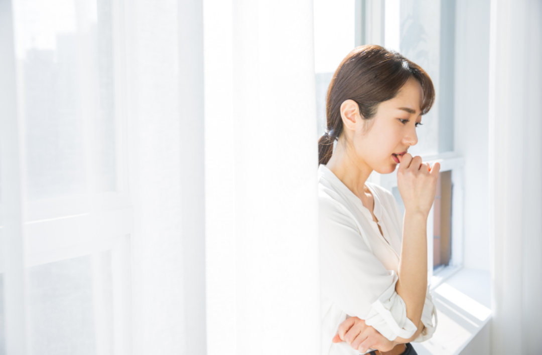 한 여성이 걱정이 가득한 표정으로 손톱을 입에 물고 있다.