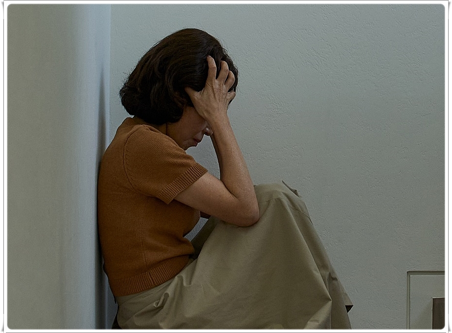 벽에 기대 앉은 채 두손으로 얼굴을 감싼 여성의 옆모습