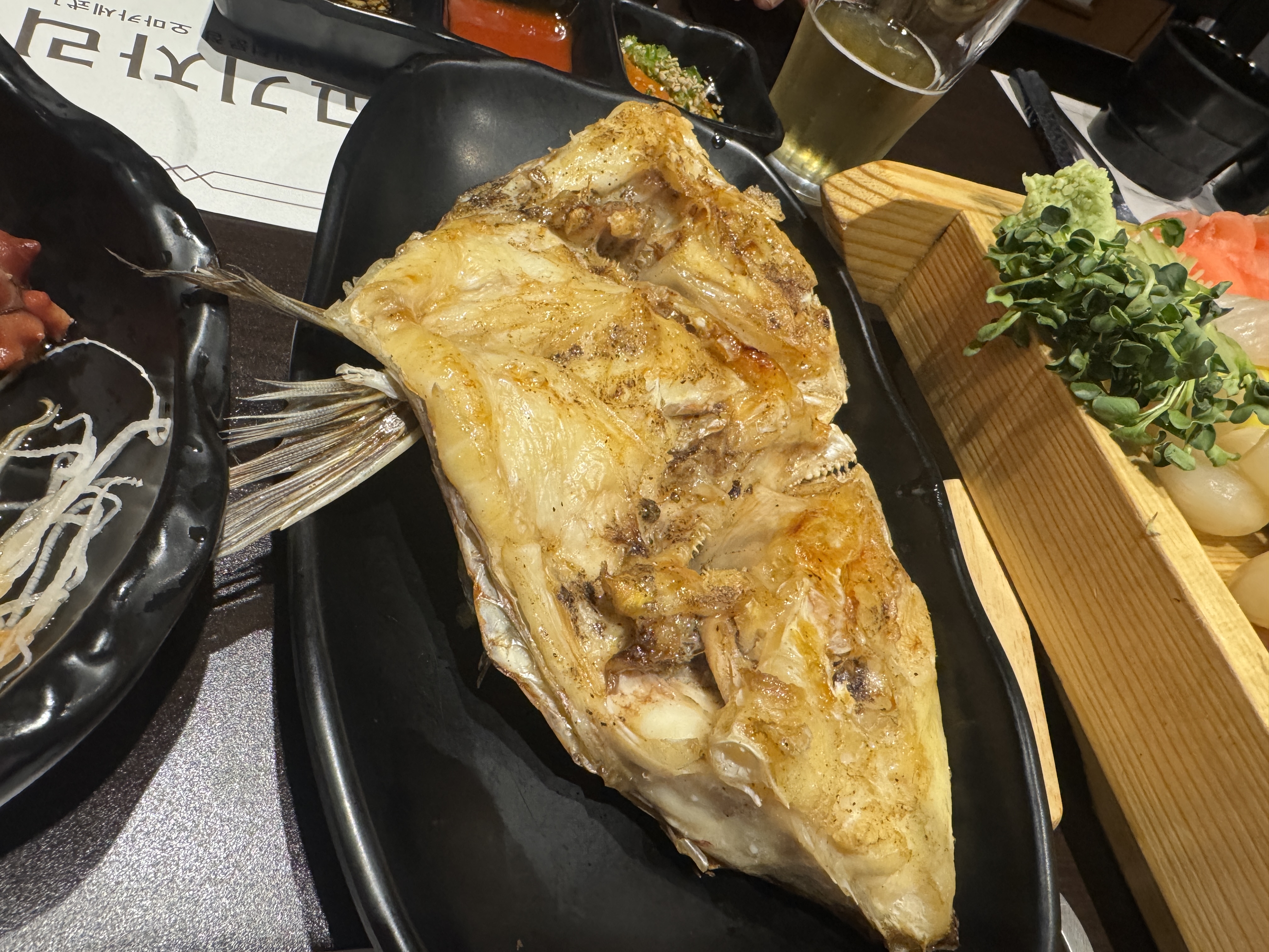 물고기 자리 논현점 숙성회 코스에 포함된 도미머리구이. 노릇하게 구워진 도미 머리 부분이 검은 접시에 담겨 있다.