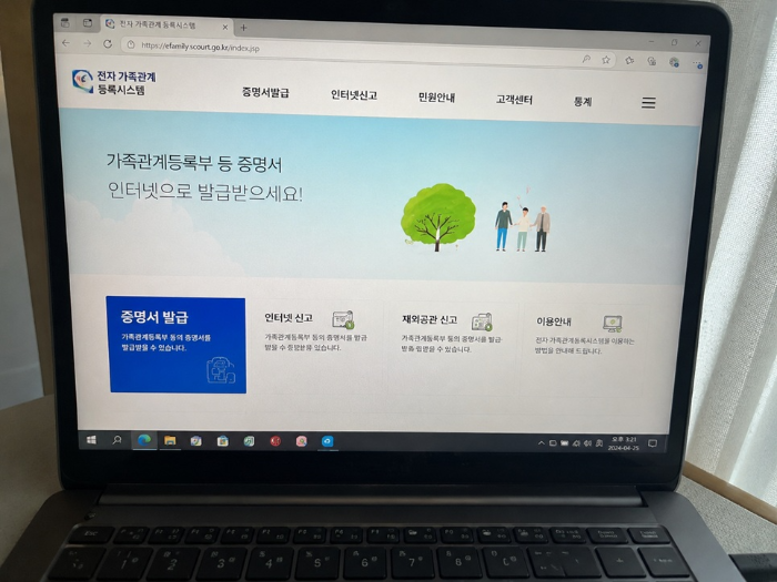 노트북에서 전자가족관계등록시스템을 확인하며 아이 통장 개설용 가족관계증명서를 준비하는 모습