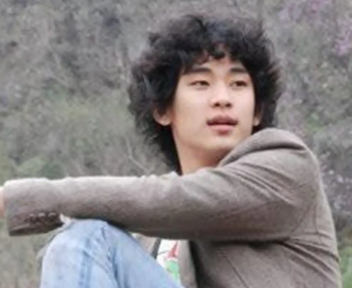 김수현- 곱슬한 머리 갈색 쟈켓 청바지를 입고 앉아서 옆을 보는 김수현