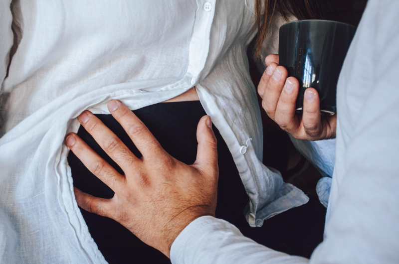 임신 중기 산모의 배 위에 손을 올린 남편과 따뜻한 차를 들고 있는 모습, 태아와의 교감 순간