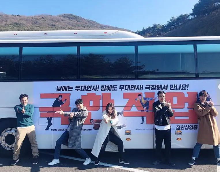 밤에피는꽃- 흰버스 앞 빨간글씨 극한직업 앞 남자배우 4명 가운데 흰롱코트 검은 바지르 긴머리를 내리고 총쏘는 포스를 하고 있는 이하늬